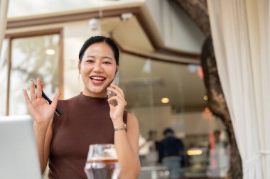 Güzel, kendine güvenen Asyalı bir kadın şehirde bir kafede çalışırken telefonla konuşuyor. Serbest çalışan, iş kadını.
