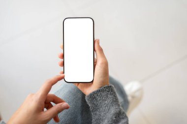 Bir kadının üst görüntüsü beyaz ekran maketli akıllı telefonu içeride otururken ekranda dokunurken tutuyor. İnsanlar, yaşam tarzları, kablosuz teknoloji