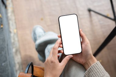 Bir kadının üst görüntüsü kapalı bir yerde oturur ve arka planda bulanıklık olan beyaz ekran maketli bir akıllı telefonu tutar. İnsanlar ve kablosuz teknoloji kavramları