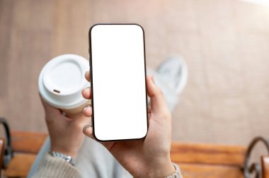 Bir kadının elinde beyaz ekran modeli olan bir akıllı telefonun üst görüntüsü. Bir kadın elinde kahve fincanı ve akıllı telefon tutuyor. İnsanlar, yaşam tarzı, kablosuz teknoloji