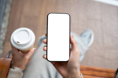 Bir kadının elinde beyaz ekran modeli olan bir akıllı telefonun üst görüntüsü. Bir kadın elinde kahve fincanı ve akıllı telefon tutuyor. İnsanlar, yaşam tarzı, kablosuz teknoloji