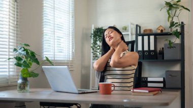 Rahatsız, yorgun, Asyalı bir iş kadını ofisinde masasında oturur, boynuna masaj yapar, uzun bir iş gününden dolayı yorgun ve ağrılı hisseder. Ofis sendromu, sağlık hizmetleri