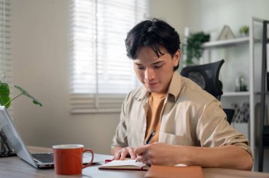 Sıradan giysiler içinde odaklanmış, zeki bir Asyalı işadamı iş fikirlerini bir kitaba yazıyor, ofisinde masasında çalışıyor..