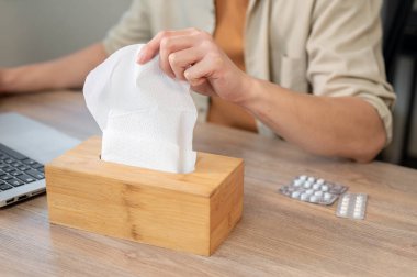 Ofisteki masasında çalışırken ahşap mendil kutusundan mendil almaya çalışan ve nezle veya burnu akan bir adamla savaşan bir adamın yakın çekimi. Sağlık, sağlık, hastalık