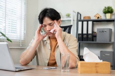 Yorgun, sağlıksız Asyalı bir işadamı çalışma masasında gözleri kapalı, baş ağrısı ya da grip ile boğuşurken çalışmaya çalışır. Sağlık, sağlık, hastalık