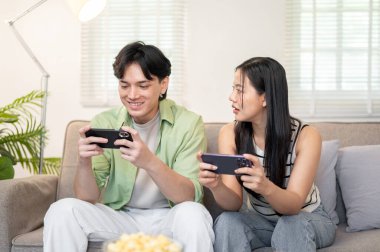 Mutlu bir Asyalı çift akıllı telefonlarıyla cep telefonu oyunu oynamaktan ve hafta sonları evde vakit geçirmekten hoşlanır. ev hayatı, yaşam tarzları, boş zaman aktiviteleri