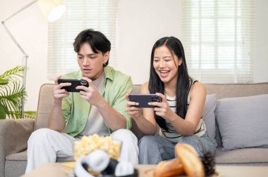 Mutlu bir Asyalı çift akıllı telefonlarıyla cep telefonu oyunu oynamaktan ve hafta sonları evde vakit geçirmekten hoşlanır. ev hayatı, yaşam tarzları, boş zaman aktiviteleri