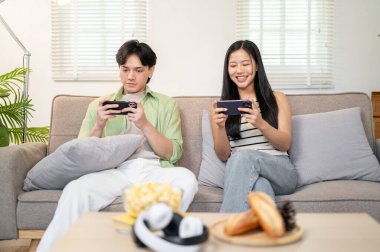 Mutlu bir Asyalı çift akıllı telefonlarıyla cep telefonu oyunu oynamaktan ve hafta sonları evde vakit geçirmekten hoşlanır. ev hayatı, yaşam tarzları, boş zaman aktiviteleri