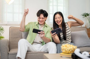 Neşeli, mutlu bir Asyalı çift akıllı telefonlarıyla yarış oyunu oynamaktan ve evde eğlenmekten hoşlanır. keyif, rekabet, eğlence, bağlanma, eğlence