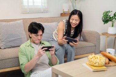 Neşeli, mutlu bir Asyalı çift akıllı telefonlarıyla yarış oyunu oynamaktan ve evde eğlenmekten hoşlanır. keyif, rekabet, eğlence, bağlanma, eğlence