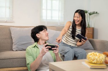 Neşeli, mutlu bir Asyalı çift akıllı telefonlarıyla yarış oyunu oynamaktan ve evde eğlenmekten hoşlanır. keyif, rekabet, eğlence, bağlanma, eğlence