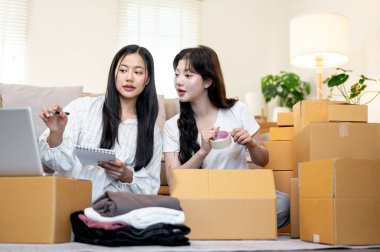 İki çekici Asyalı bayan dükkan sahibi karton kutulara şeker koyarken müşterilerine gönderilecek eşyaları hazırlarken konuşuyor. Online alışveriş, e-ticaret, küçük işletme