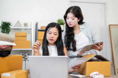 İki odaklı Asyalı kadın girişimci ofiste birlikte çalışarak, başlangıç işleri kapsamında online alışveriş sitelerinde siparişleri tartışıyor ve kontrol ediyorlar. e-ticaret konsepti