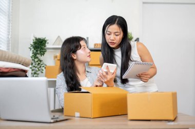 İki odaklanmış Asyalı kadın envanter çalışanı ofiste birlikte çalışıyorlar, nakliye malzemelerini tartışıp kontrol ediyorlar. Girişim işi, e-ticaret, çevrimiçi mağaza