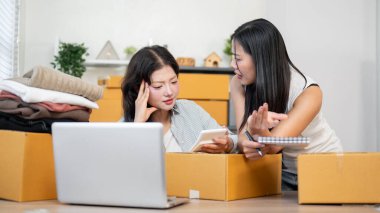 İki ciddi, stresli Asyalı kadın envanter çalışanı, web sitesindeki siparişleri kontrol ettikten sonra, ofiste birlikte çalıştıktan sonra stok ürünlerinin eksikliğinden endişe duyuyorlar..