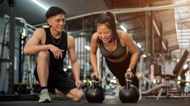 Kararlı bir Asyalı bayan müvekkil spor salonunda profesyonel bir fitness eğitmeni tarafından eğitiliyor, antrenmanının bir parçası olarak kettlebell ile şınav çekiyor. Sağlıklı yaşam tarzı, kas yapısı