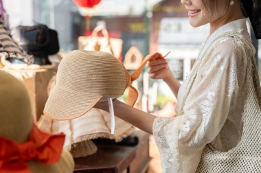 Mutlu bir Asyalı kadının yakın plan çekimi şapkacıda ürünleri dikkatlice seçmesi, alışveriş çılgınlığının keyfini çıkarması. moda, yaşam tarzı, alışveriş, tatil