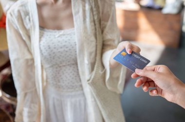 Tatmin olmuş bir Asyalı kadın müşterinin alışveriş yaparken alışveriş yapması için kredi kartını bir kasiyere vermesi..