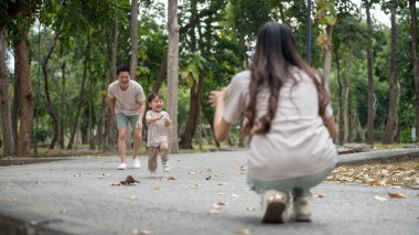 Neşeli, masum bir Asyalı çocuk babasının parkında babasıyla kovalamaca oynarken annesine koşuyor. Açık hava aktivitesi, aile anı, çocukluk, ebeveynlik