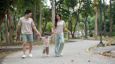 Şefkatli ve mutlu Asyalı ebeveynler, halka açık bir parkta birlikte sabah egzersizinin tadını çıkarırken, oğullarının elini tutuyorlar. Açık hava aktivitesi, aile anı, çocukluk, ebeveynlik