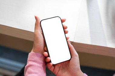 Bir kafe 'de akıllı telefonunu kullanırken rahatlayan bir kadının yakın çekimi. Elinde tutulan telefon, beyaz bir ekran modeli içeriyor..