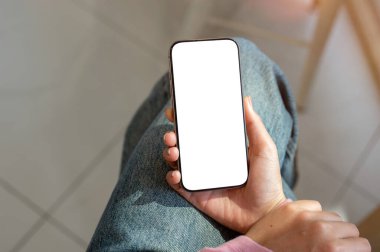 Kapalı alanda oturan ve akıllı telefonunu kullanan bir kadının yakın plan görüntüsü. Beyaz ekran maketi olan bir akıllı telefon