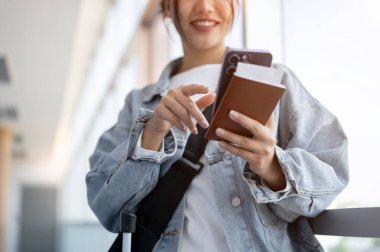 Havaalanı terminali koridorunda yolcu alımını bekleyen Asyalı bir bayan yolcunun yakın çekimi, akıllı telefonundan sohbet okuyor. seyahat, kablosuz teknoloji, yaşam tarzı