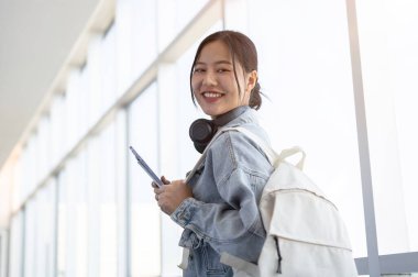 Kot ceketli ve sırt çantalı güzel bir Asyalı bayan gezgin havaalanı koridorunda yürürken kameraya gülümsüyor. seyahat, tatil, özgürlük, yaşam tarzları