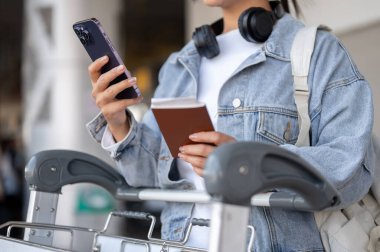 Kot ceketli bir bayan gezginin yakın plan fotoğrafı havaalanının buluşma noktasında elinde bir pasaport ve akıllı bir telefonla taksisini bekliyor. insanlar ve ulaşım kavramları