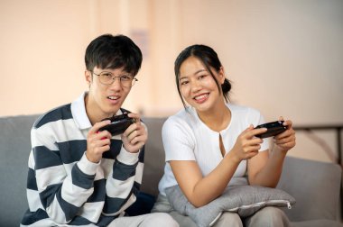 İki heyecanlı, neşeli Asyalı genç arkadaş evdeki kanepede video oyunu oynayarak eğleniyorlar. boş zaman aktivitesi, eğlence, hobiler