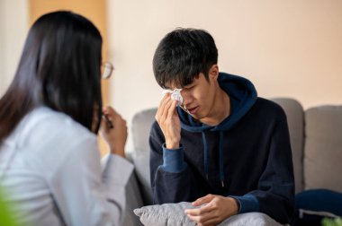 Stresli, ağlayan Asyalı genç bir adam klinikte psikoloğuyla konuşuyor, sağlık kontrolü sırasında ruhsal bir çöküntü yaşıyor. ruh sağlığı kavramı