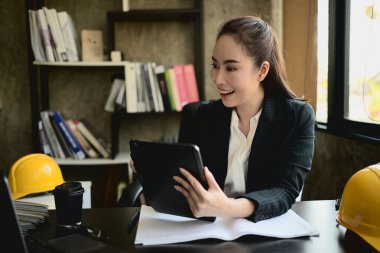 Güzel, başarılı bir Asyalı kadın mühendis masasında çalışıyor, projesini dijital tablette gözden geçiriyor..