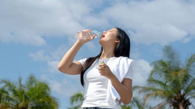 Güzel bir kadın parkta koştuktan sonra omzunun üstünden havluyla su şişesinden su içiyor..