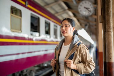 Çantalı güzel Asyalı kadın tren istasyonuna bakıyor. Tren istasyonunda veya tren istasyonunda bekleyen yolcu..