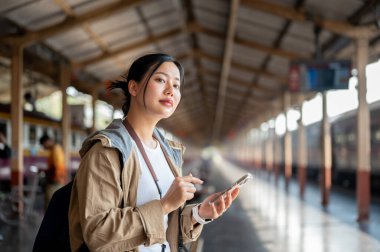 Güzel Asyalı kadın telefonu tutarken önüne bakıyor tren istasyonuna ya da tren istasyonuna varmasını bekliyor..