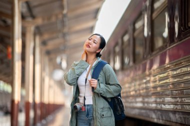 Asyalı bir kadın, tren istasyonu ve tren vagonunun bulanık geçmişiyle terini silerken rahatsız görünüyor..