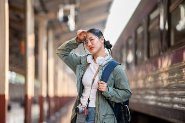 Asyalı bir kadın istasyonda terini silerken yorgun görünüyor. Tren vagonunun, tren istasyonunun ya da tren istasyonunun bulanık arka planına sahip..