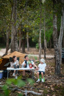 Üç kişilik aile, bir oğlu olan anne ve baba, ormanda kamp yaparken mutlu görünüyorlar. Aile gezisi, açık hava aktivitesi.