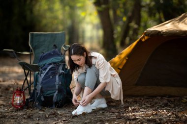 Kadın, ormanda kamp çadırının önünde ayakkabı bağını bağlıyor. Kamp, açık hava aktiviteleri..