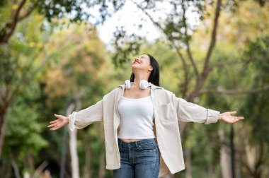 Mutlu bir Asyalı kadın parkta kollarını açmış temiz hava soluyor. Doğada dinlenme, açık hava aktivitesi, yeşil orman parkı..