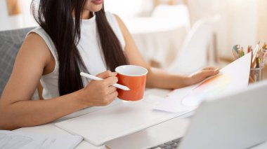 Belgeyi okurken portakallı seramik bardağı stille tutan bir elin yakın çekimi. İç Tasarımcı veya Grafik Tasarımcısı.