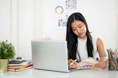 Asyalı bir kadın elindeki basılı renk çizelgelerinden ya da renk paletlerinden renk seçiyor. Ofiste çalışan İç mimar veya Grafik Tasarımcı.