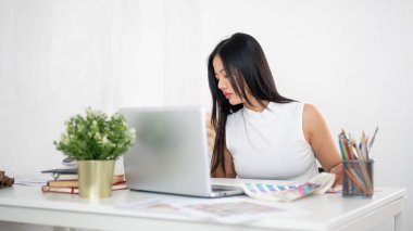 Asyalı bir kadın masadaki basılı renk çizelgesine ya da renk paleti dokümanlarına bakıyor. Ofiste çalışan İç mimar veya Grafik Tasarımcı.