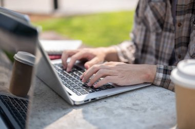 Parktaki beton bir masada arkadaşlarıyla ya da iş arkadaşıyla otururken dizüstü bilgisayarda yazan bir çift eli kapat. Grup projesi, Çalışma ya da Açık havada Çalışma.
