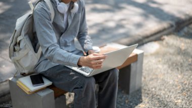 Asyalı bir adamın dizüstü bilgisayarına dokunup kaldırım kenarındaki bankta otururken resmini çek. Boş zaman geçirmek, çalışmak ya da dışarıda çalışmak..