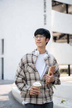 Gözlüklü Asyalı bir adam elinde kitaplarla bir kahve fincanı tutuyor ve binanın önünde dikilirken kafasını çeviriyor. Dışarı çıkmak ya da bir yerlere gitmek..