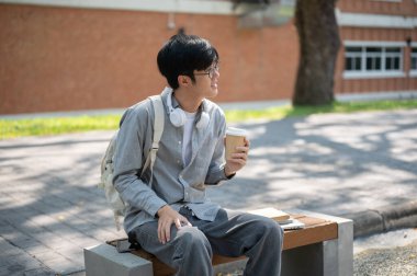 Gözlüklü Asyalı bir adam elinde kahve fincanı, kaldırım bankında otururken başka tarafa bakıyor. Boş zaman geçirmek, Serinlemek.