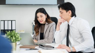 Bayan ofis çalışanı, erkek iş arkadaşına dizüstü bilgisayardaki verileri gösteriyor ve açıklıyor. İş adamı ve iş kadını ofiste tartışıyorlar..