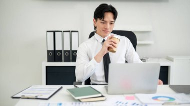 İş adamı ya da erkek ofis çalışanı elinde kahve, dizüstü bilgisayarına bakarken tatmin olmuş görünüyor..