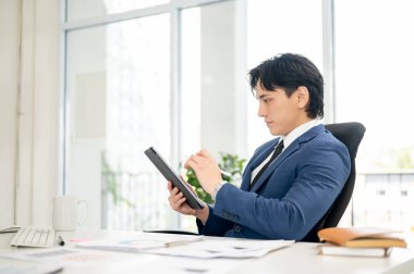 İş adamı ya da erkek ofis çalışanı dijital tablete sağ eliyle bakıyor ve sol elinde bir stilus kalem tutuyor. Ofisteki çalışma masasında oturmak..